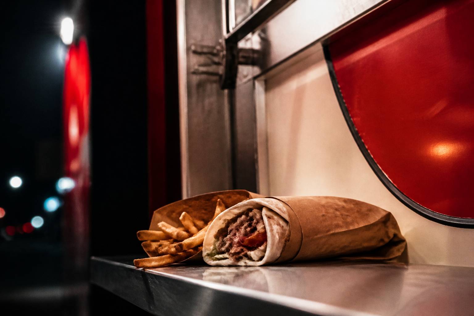 Sandwich enroulé dans du papier kraft posé sur un comptoir avec des frites