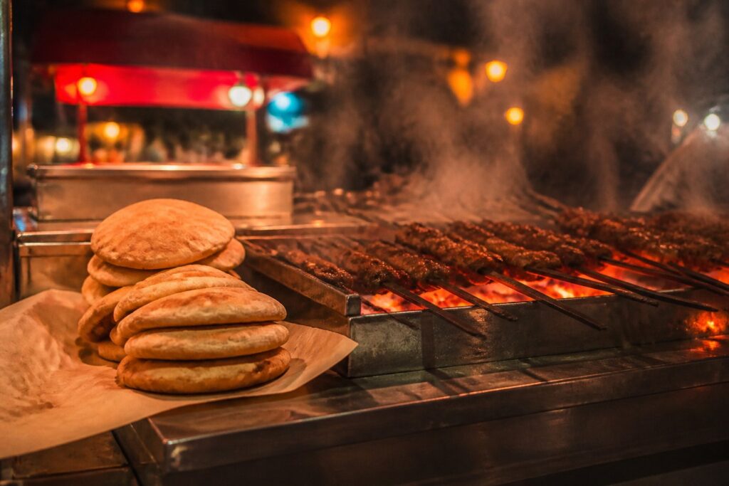 Étal de street food nocturne avec brochettes grillées et pains dorés